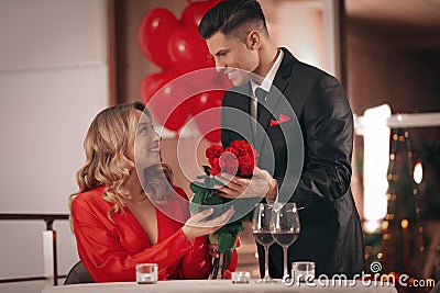 Man presenting roses to his beloved woman in restaurant at Valentine`s day dinner Stock Photo