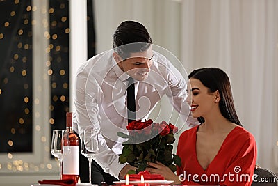 Man presenting roses to his beloved woman in restaurant. Romantic Valentine`s day dinner Stock Photo