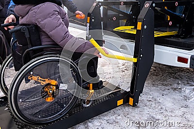 A man presses a button on the control panel to pick up a woman in a wheelchair in a taxi for the disabled. Black lift specialized Stock Photo