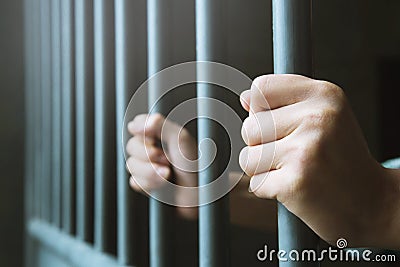 Man in prison hands of behind hold Steel cage jail bars. Stock Photo