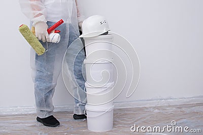 A man in protective clothing, with paint rollers in his hands, put four buckets on top of each other, against the background of a Stock Photo