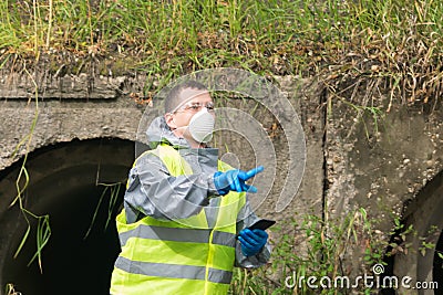A man in a protective suit and mask with a phone in his hands shows his finger at the site of the epicenter of the environmental Stock Photo