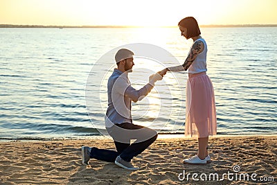 Man putting beautiful engagement ring on hand of his beloved near river Stock Photo