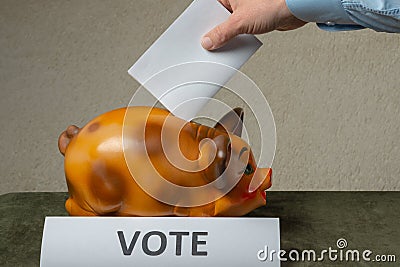 Man putting his vote into piggi-bank on table Stock Photo