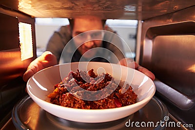 Man Putting Leftover Chili Into Microwave Oven To Cook Stock Photo