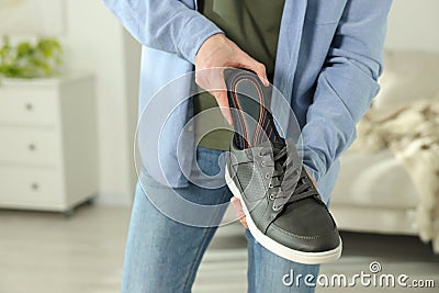 Man putting orthopedic insole into shoe indoors, closeup. Space for text Stock Photo