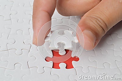 Man is putting a single part of a white puzzle in its place on the red background. Stock Photo