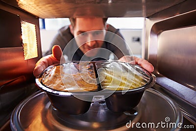 Man Putting TV Dinner Into Microwave Oven To Cook Stock Photo