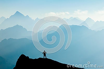 Man reaching summit after climbing and hiking enjoying freedom and looking towards mountains silhouettes panorama during Stock Photo