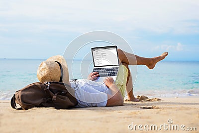 Man reading email on laptop while relaxing on beach Stock Photo