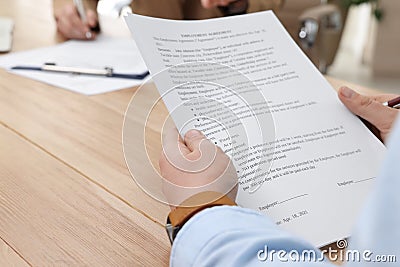 Man reading employment agreement at table in office, closeup. Signing contract Stock Photo