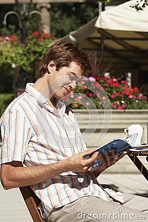 Man Reading Guidebook At Outdoor Cafe Stock Photo