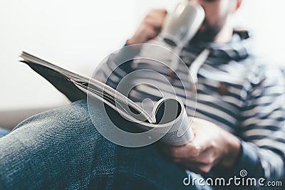 Man reading magazine or newspaper and drinking coffee while relaxing on sofa Stock Photo