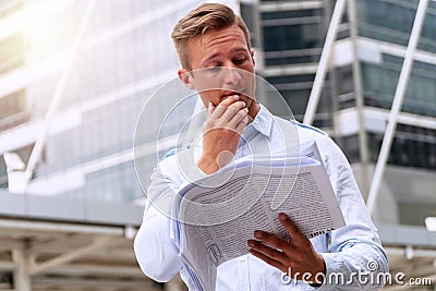 Man reading newspaper feeling serious while standing in urban background. Handsome men holding newspaper in his hand with Stock Photo