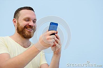 Man with a red beard looks into the phone with surprise and ecstasy a bright summer photo on a blue background Stock Photo