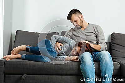 A man regrets a girl who has a stomach ache. Sit on a gray sofa. Abdominal pain, menstrual cycle, women`s problems Stock Photo