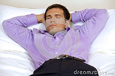 Man relaxing in hotel room with hands behind head, eyes closed Stock Photo