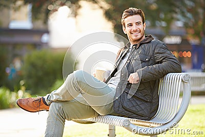 Man Relaxing On Park Bench With Takeaway Coffee Stock Photo