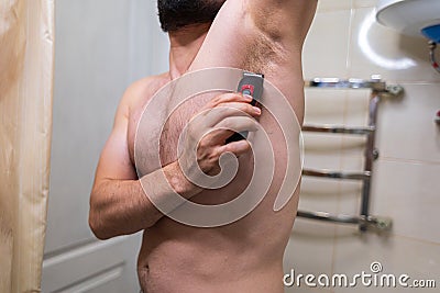 A man removes unwanted hair from his body using an electric razor. A man with an athletic figure in the bathroom Stock Photo