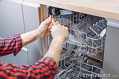 Man repairing dishwasher. Male hand with screwdriver installs kitchen appliances Stock Photo