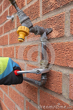 Man replacing burst copper water pipe outdoors. Unscrewing a brass connector with a spanner Stock Photo