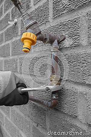 Man replacing burst copper water pipe outdoors. Unscrewing a brass connector with a spanner wrench. Stock Photo