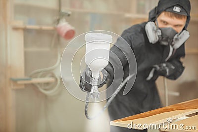Man in respirator mask painting wooden planks at workshop. Stock Photo