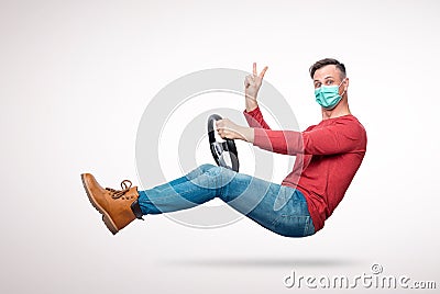 Man in a respiratory mask with a car steering wheel gives a victory sign with his hand. Attention virus concept Stock Photo