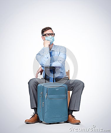 Man in a respiratory mask, glasses, a shirt and a tie sits with a suitcase waiting for a flight. Pandemic Travel concept. Stock Photo