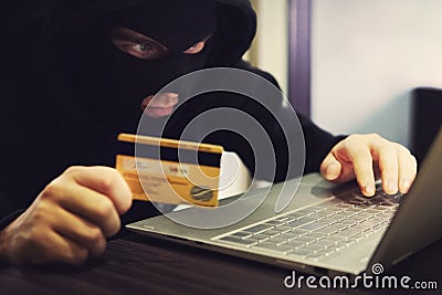 Man in robber mask and hood misappropriates personal bank data. Cyber fraudster attacks online banking system. Hacker Stock Photo