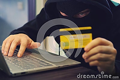 Man in robber mask uses internet, bank account and credit facilities. Phishing attack by male with hidden face. Hacker enters Stock Photo