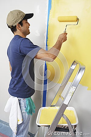 Man With Roller Applying Yellow Paint On A Wall Stock Photo