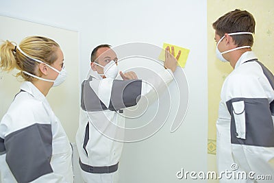 Man rubbing down wall apprentices watching Stock Photo