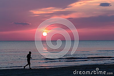 Man running on the beach while the sun is setting Stock Photo