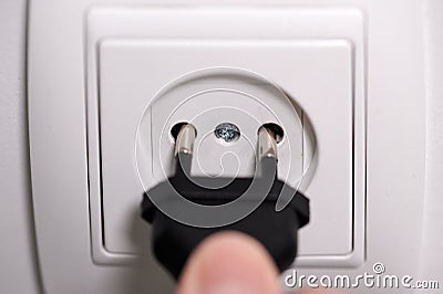 A man`s finger plugging a plug into a wall socket Stock Photo