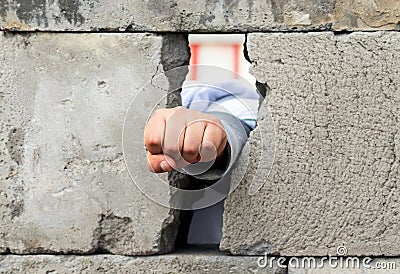 The man`s hand squeezed into a fist smashes through the wall of gray concrete blocks. Symbol of struggle, victory and liberation Stock Photo