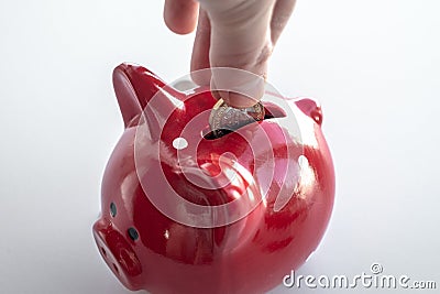 A man`s hand drops a hexagonal English coin into a piggy bank. The concept of accumulating money, bank account, savings Stock Photo