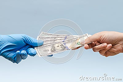 Man`s hand giving money dollars to hand in blue surgical glove, nurse or doctor. Corruption in medicine field Stock Photo