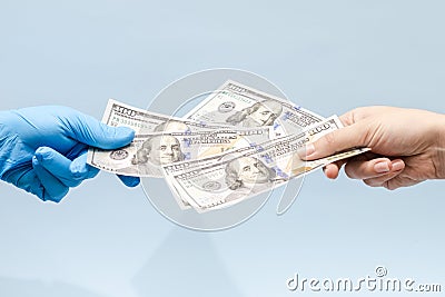 Man`s hand giving money dollars to a hand in blue surgical glove, nurse or doctor. Corruption in medicine field Stock Photo