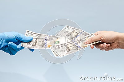 Man`s hand giving money dollars to hand in blue surgical glove, nurse or doctor. Corruption in medicine field Stock Photo