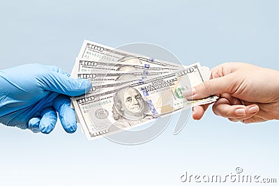 Man's hand giving money (dollars) to hand in blue surgical glove, nurse or doctor. Corruption in medicine field Stock Photo