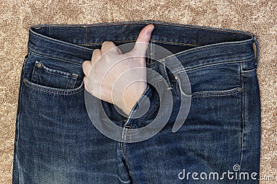 A man`s hand, with his thumb raised, protrudes from the fly of his jeans. Stock Photo