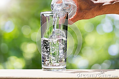 Man`s hand holding drinking water bottle water and pouring water into glass on wooden tabletop on blurred green bokeh background Stock Photo