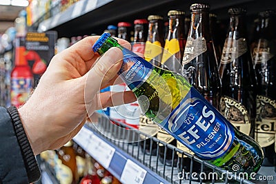 Man`s hand is holding Efes beer bottle from supermarket shelf. Various bottles of beer on shelf in store. Minsk, Belarus, 2022 Editorial Stock Photo