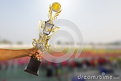 Man`s hand holding golden winner trophy cup on blurred sport stadium Stock Photo