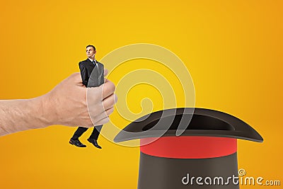 Man`s hand holding tiny businessman and putting him in black top-hat on amber background with some copy space above the Stock Photo