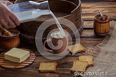 A man`s hand pours milk into a cup on the background of burlap and a wooden background. Around scattered crackers Stock Photo