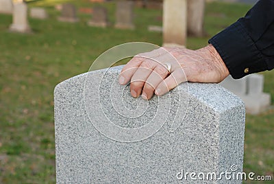 Man's hand resting on headstone Stock Photo