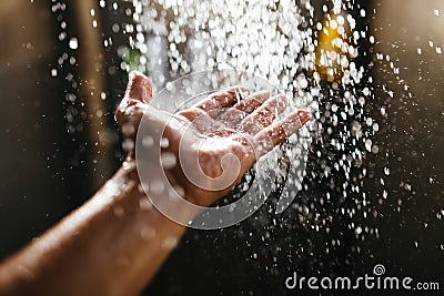 A man`s hand in a spray of water in the sunlight against a dark background. Water as a symbol of purity and life Stock Photo