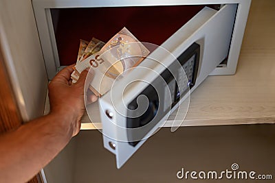 Man's hand stuffs euro bills into a small safe Stock Photo